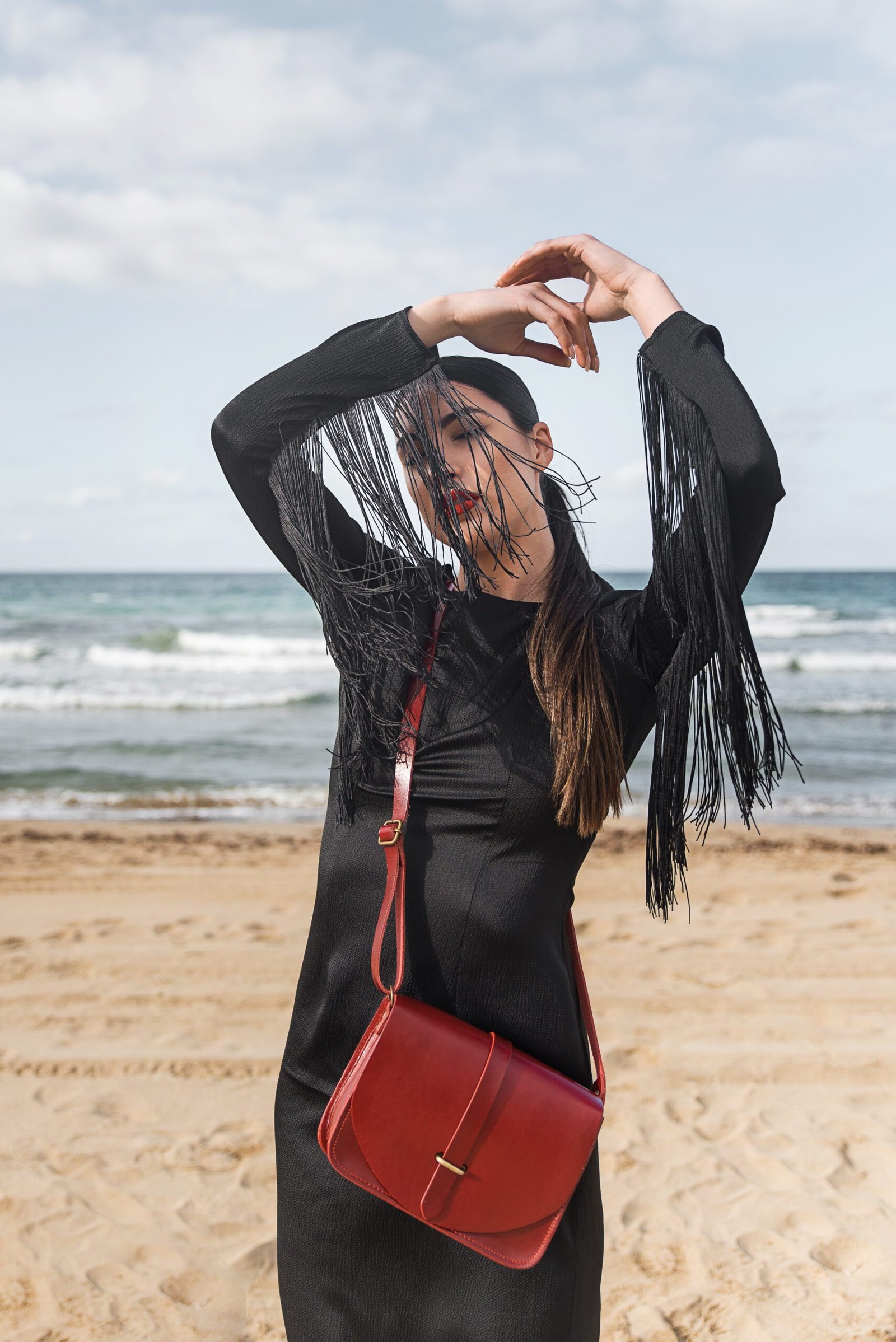 Woman wearing red leather flap shoulder bag crossbody on the beach, Jirakis Handcrafted Leather, Crete.