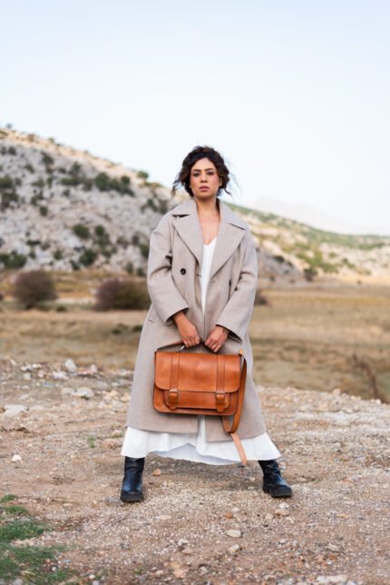 Woman in neutral coat holding structured leather briefcase with flap and buckles, handcrafted by Jirakis Handcrafted Leather in Crete.