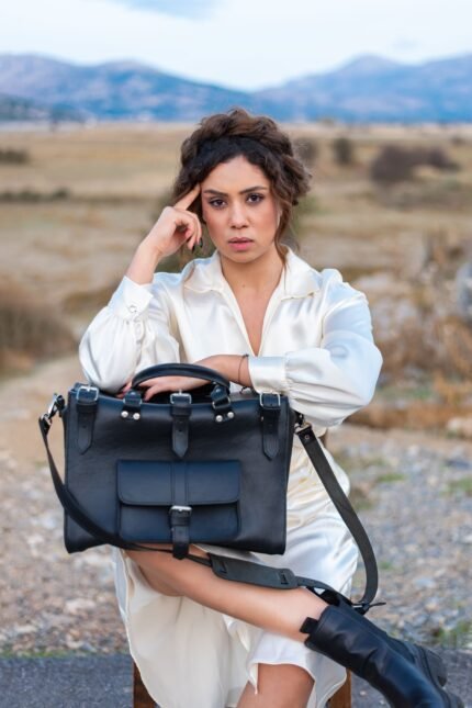 Woman holding black Spartan Nomad leather travel bag with buckles, handcrafted by Jirakis Handcrafted Leather in Crete.