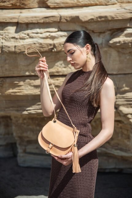 Woman wearing a natural leather saddle crossbody bag with buckle and tassel, Jirakis Handcrafted Leather