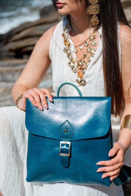 Model holding a blue leather flap backpack with buckle, handcrafted by Jirakis Handcrafted Leather.