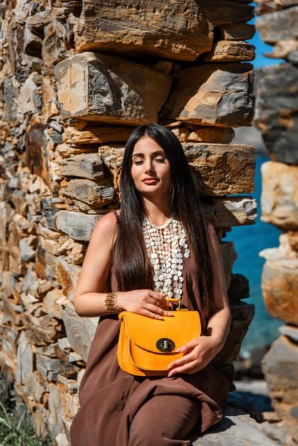 woman holds yellow Leather flap shoulder bag for women with classic structured shape and adjustable strap by Jirakis Leather.